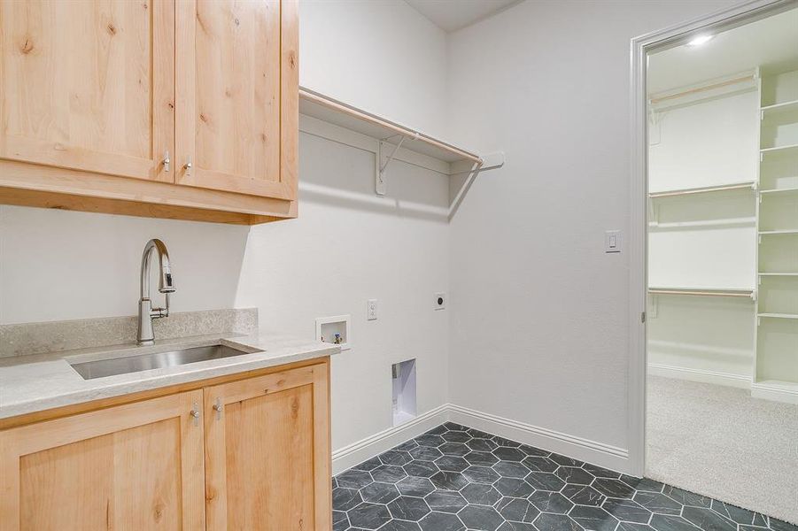 Utility room with custom cabinetry, sink, and tile floors with access to the primary bedroom closet