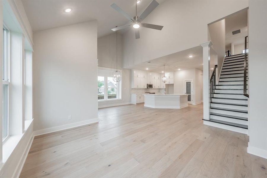 Unfurnished living room with recessed lighting, a chandelier, stairway, light wood finished floors, and high vaulted ceiling