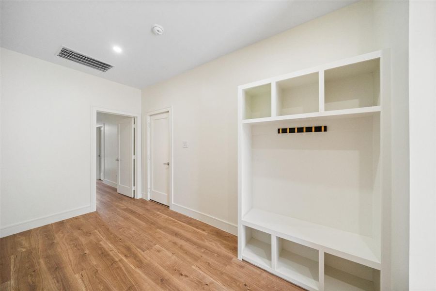 A bright entry with wide plank engineered wood floors, neutral walls, and mudroom bench.