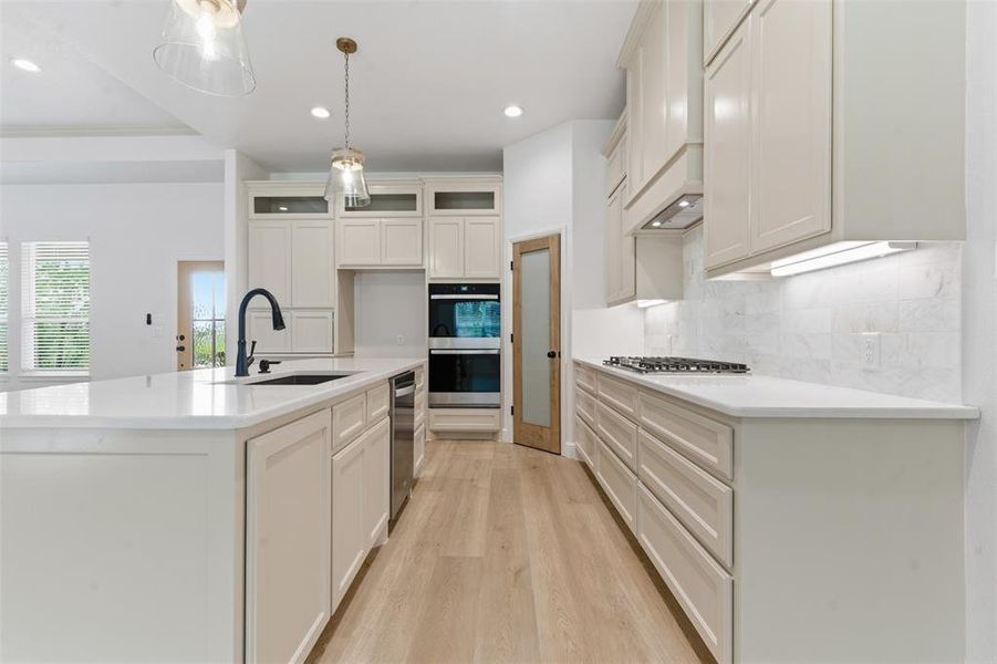 Kitchen with light wood finished floors, light stone countertops, an island with sink, glass insert cabinets, and recessed lighting Kitchen with light wood finished floors, light stone countertops, an island with sink, glass insert cabinets, and recessed lighting