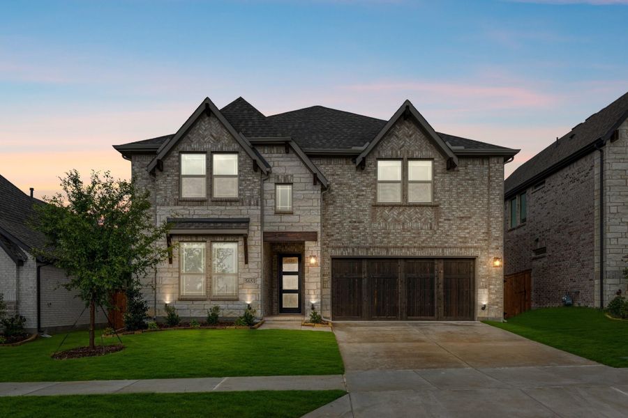 Two-story brick and stone home with two-car garage, dark roof, and green front lawn at dusk Two-story brick and stone home with two-car garage, dark roof, and green front lawn at dusk