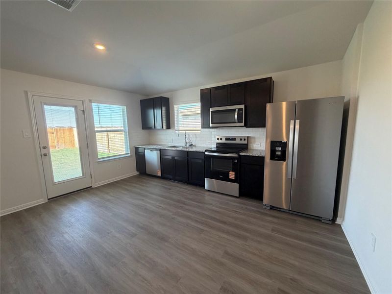 Kitchen with appliances with stainless steel finishes, light countertops, decorative backsplash, dark wood-style flooring, and lofted ceiling