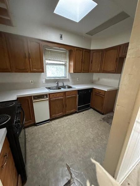 Kitchen featuring brown cabinets, light countertops, a skylight, and black appliances