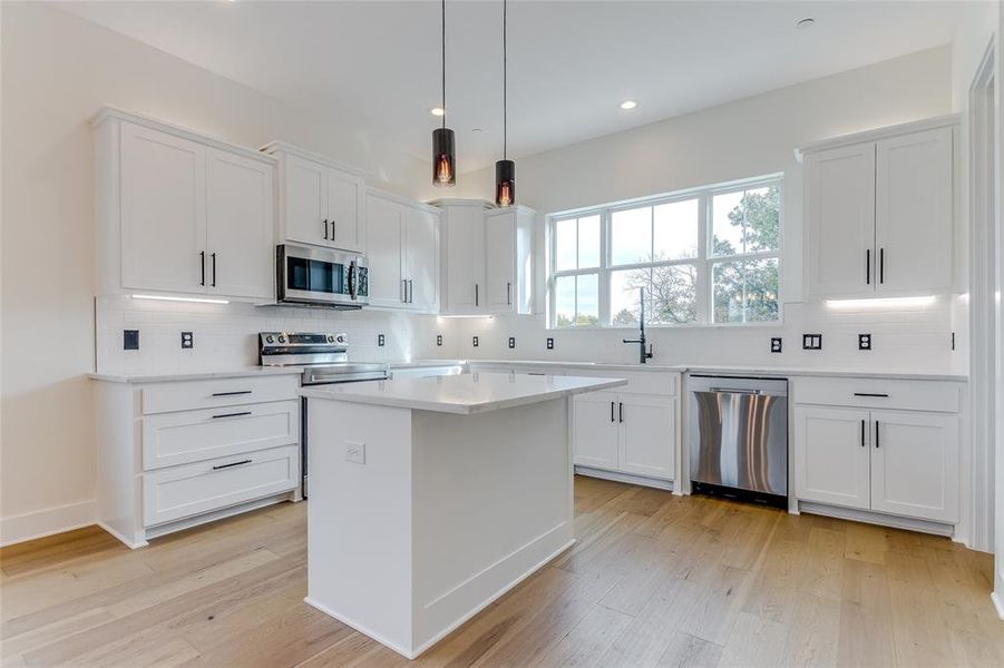 Kitchen with white cabinets, hanging light fixtures, appliances with stainless steel finishes, and light hardwood / wood-style flooring