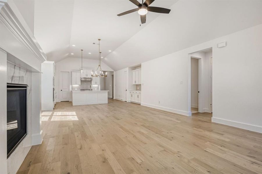 Unfurnished living room featuring suspended lighting, light wood-type flooring, a high end fireplace, a ceiling fan, and vaulted ceiling
