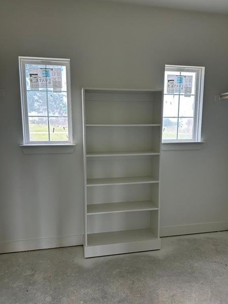 Built-in white shelving unit with five tiers, flanked by two double-hung windows