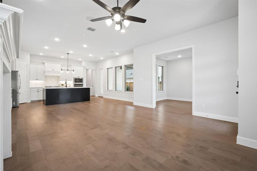 Spacious living area featuring light hardwood flooring, a contemporary fireplace with a stone surround and classic mantel, and a ceiling fan with integrated lighting