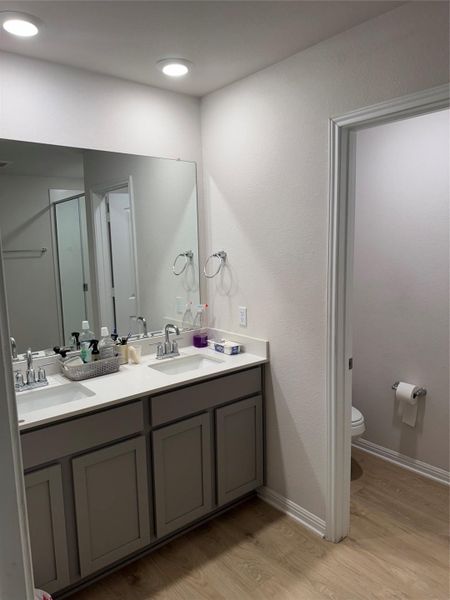 Full bath with double vanity, light wood-style flooring, and a stall shower