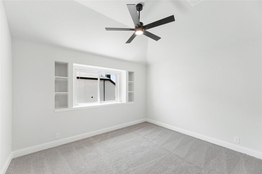 Empty bedroom with vaulted ceiling, black ceiling fan, built-in shelves, and carpet flooring Empty bedroom with vaulted ceiling, black ceiling fan, built-in shelves, and carpet flooring