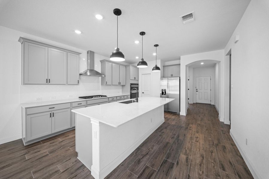 Kitchen with stainless steel appliances, wall chimney range hood, recessed lighting, an island with sink, and arched walkways Kitchen with stainless steel appliances, wall chimney range hood, recessed lighting, an island with sink, and arched walkways
