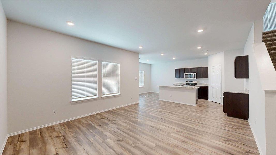 Expansive open-concept living area featuring wood-finish flooring, recessed lighting, and large windows with blinds Expansive open-concept living area featuring wood-finish flooring, recessed lighting, and large windows with blinds
