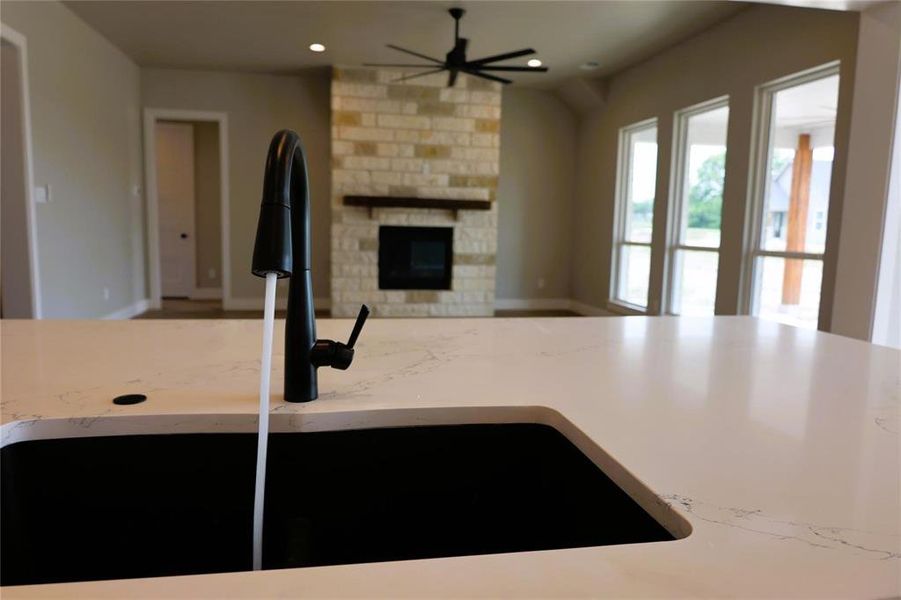 Kitchen featuring light stone counters, ceiling fan, brick wall, a stone fireplace, and sink