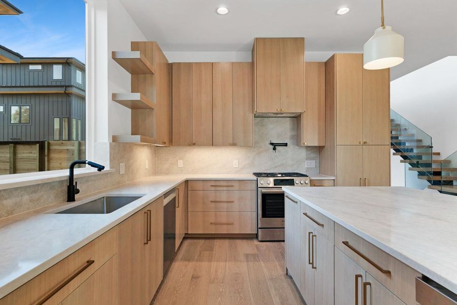 Kitchen with light brown cabinetry, plenty of natural light, open shelves, light stone countertops, and recessed lighting