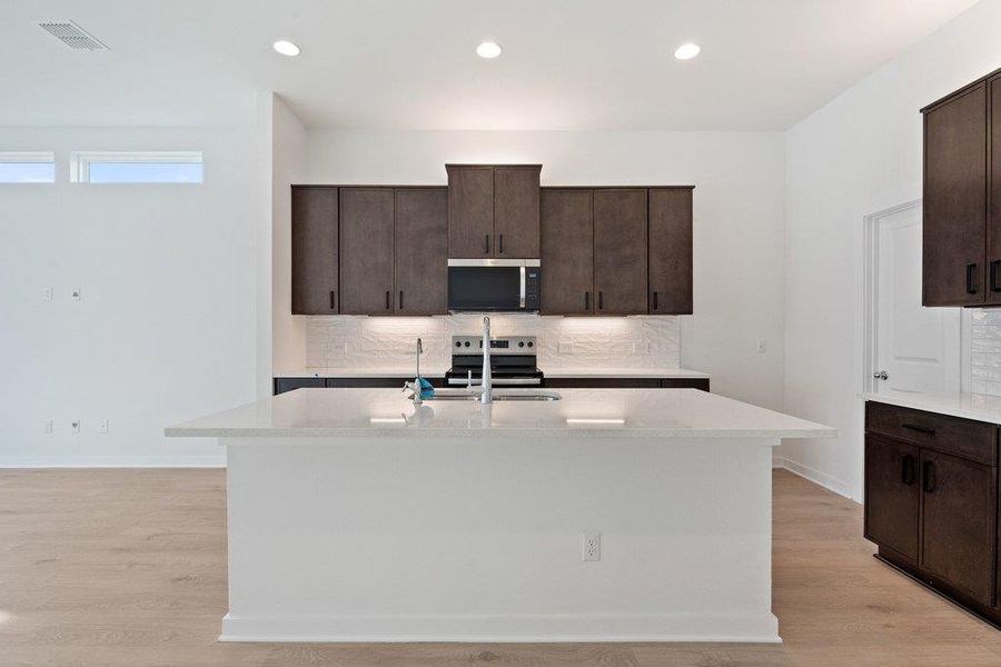 Kitchen featuring dark wood finish cabinets, tasteful backsplash, a center island with sink, stainless steel appliances, and recessed lighting