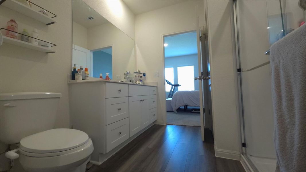 Bathroom featuring a white vanity with integrated sink, wood-finish flooring, a frameless shower enclosure, and a full-width wall mirror