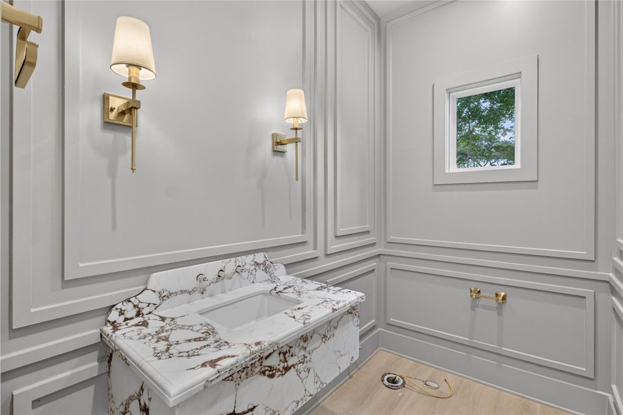 Elegantly designed for guests, this stylish powder bath showcases a striking marble pedestal sink complemented by classic wainscoting wall detailing. Elegantly designed for guests, this stylish powder bath showcases a striking marble pedestal sink complemented by classic wainscoting wall detailing.