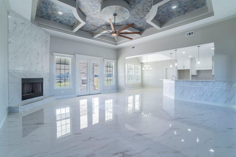 Unfurnished living room with a ceiling fan, coffered ceiling, healthy amount of natural light, a chandelier, and a fireplace