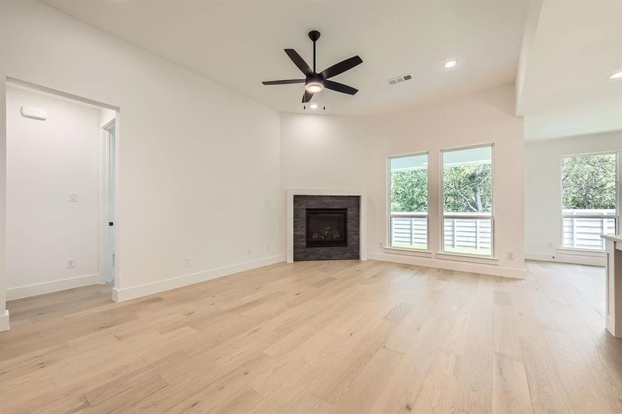 Unfurnished living room featuring light wood finished floors, baseboards, ceiling fan, a fireplace, and recessed lighting