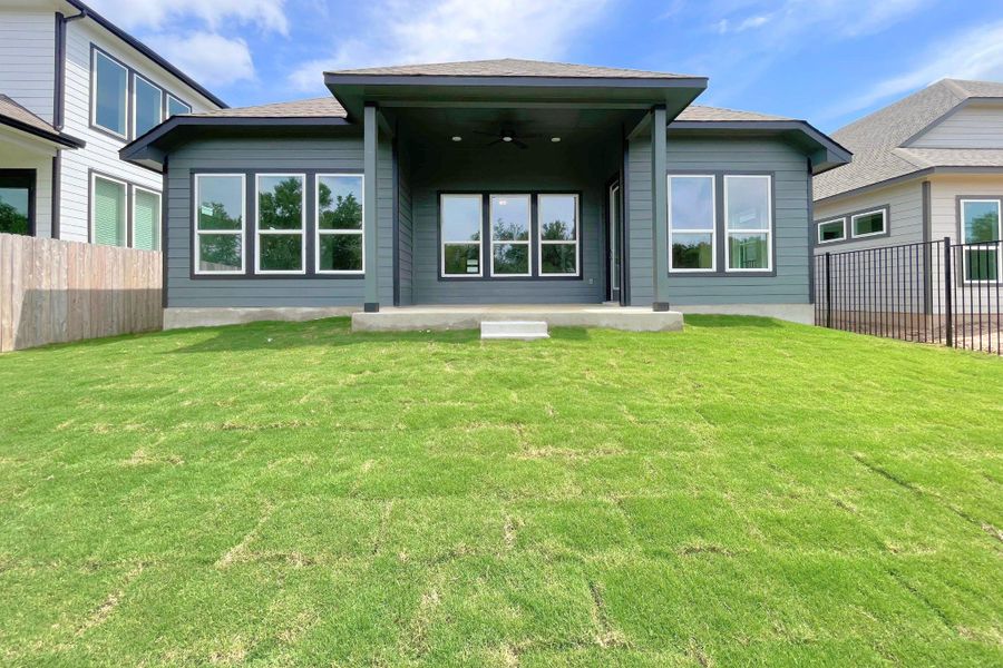 A deep-hued modern residence featuring a welcoming covered patio and a freshly laid green lawn.