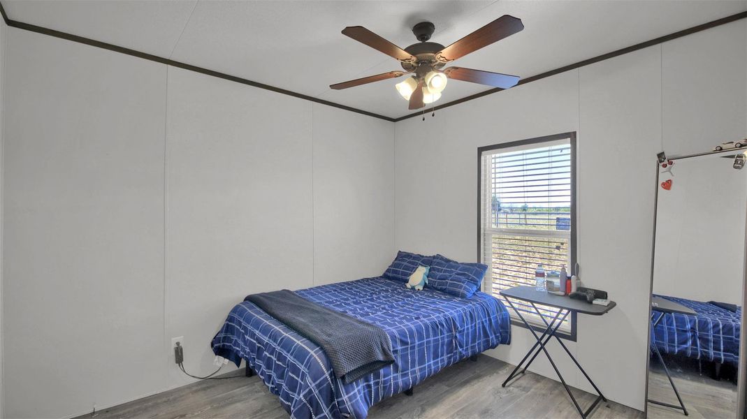 Bedroom featuring light wood-type flooring, a ceiling fan, crown molding, and a decorative wall
