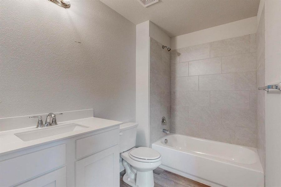 Full bathroom featuring vanity, a textured ceiling, tiled shower / bath combo, hardwood / wood-style flooring, and toilet