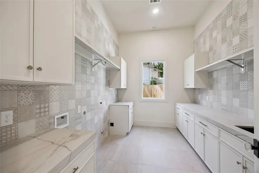 UTILITY: Exceptional laundry room is thoughtfully designed with abundant cabinetry, extensive countertop workspace, hanging area, sink, and Nantes Taj Mahal Quartzite surfaces.