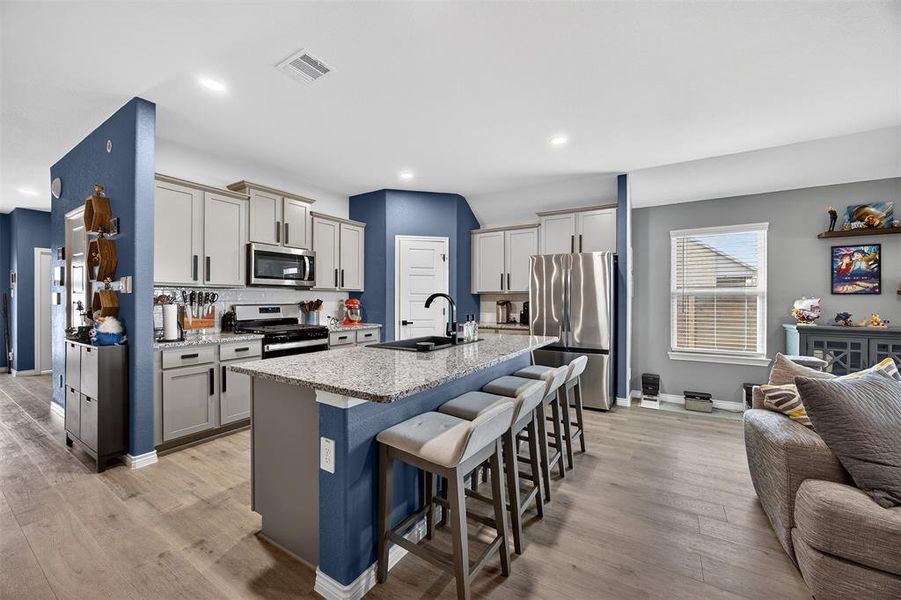 Kitchen with stainless steel appliances, a breakfast bar, open floor plan, a center island with sink, and light stone countertops