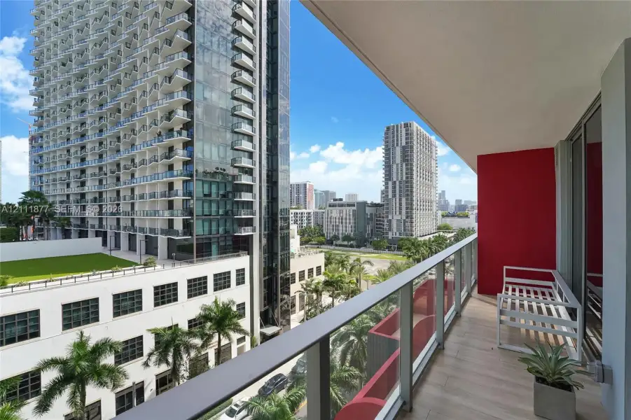 Covered private balcony with tile flooring, glass panel railing, and high-rise urban surroundings