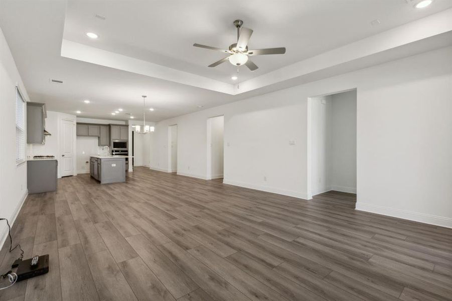 Unfurnished living room with ceiling fan with notable chandelier, dark hardwood / wood-style floors, and a raised ceiling