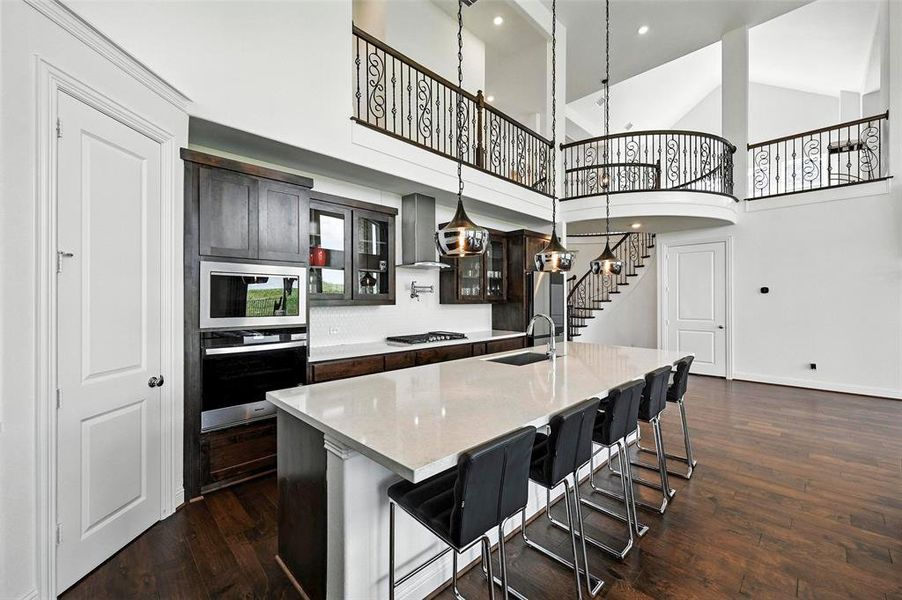 Kitchen with appliances with stainless steel finishes, wall chimney exhaust hood, an island with sink, dark wood-type flooring, and glass insert cabinets