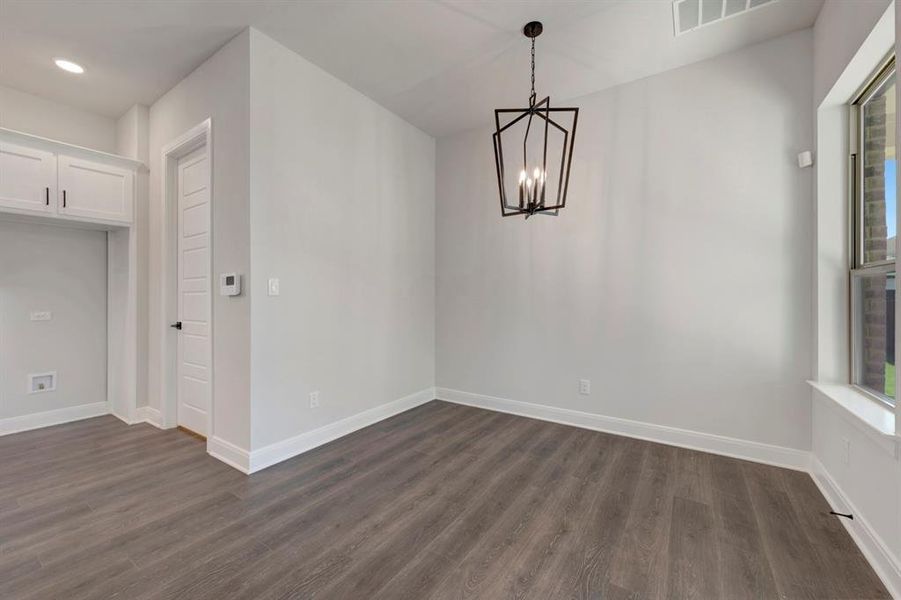 Unfurnished dining area with suspended lighting and dark wood-style flooring