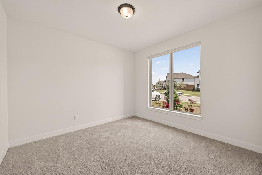 Bright home office with neutral carpeting, a large window providing natural light, and a view of a suburban street. Ideal for a bedroom or office space.