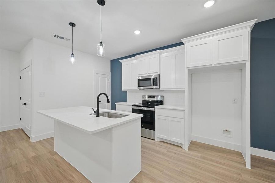 Kitchen featuring stainless steel appliances, a sink, light wood-style flooring, white cabinetry, and an island with sink