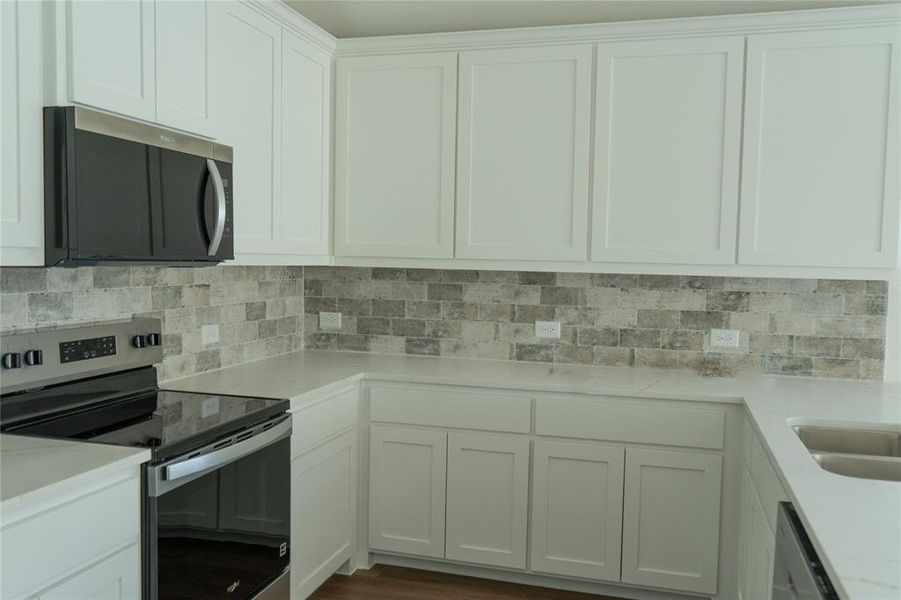 Kitchen with stainless steel appliances, decorative backsplash, white cabinetry, light stone counters, and dark wood-style floors