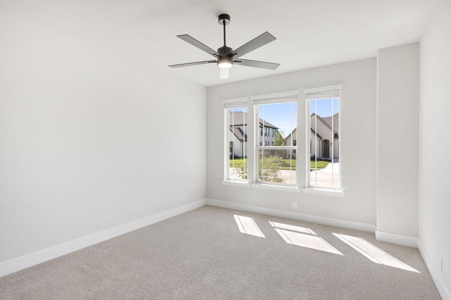 Empty bedroom with carpet flooring, ceiling fan, and three windows overlooking a neighborhood street Empty bedroom with carpet flooring, ceiling fan, and three windows overlooking a neighborhood street
