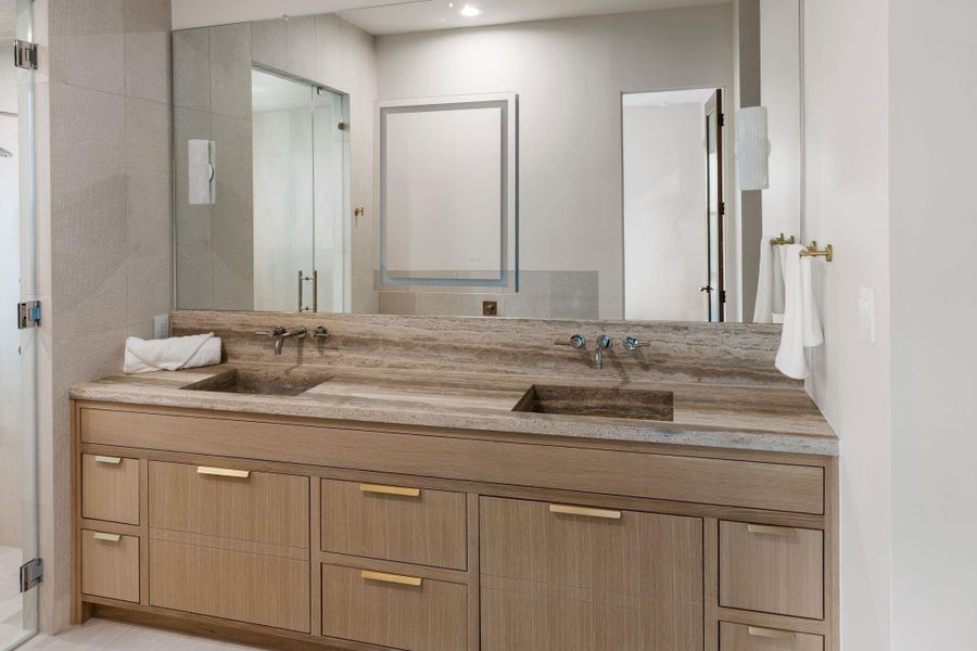 In the primary bathroom, a Travertino Classico Romano countertop with an integrated carved sink is sculpted seamlessly from a single slab, creating a refined, monolithic statement. In the primary bathroom, a Travertino Classico Romano countertop with an integrated carved sink is sculpted seamlessly from a single slab, creating a refined, monolithic statement.