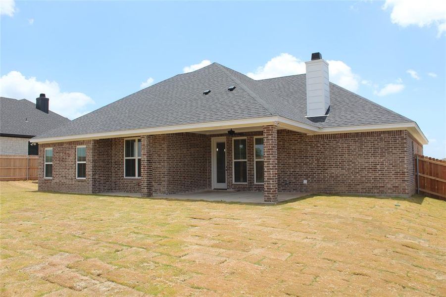 Back of house with brick siding, a chimney, a patio area, and a shingled roof Back of house with brick siding, a chimney, a patio area, and a shingled roof