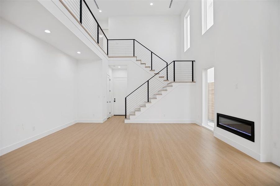 Spacious interior featuring a contemporary wood-finish flooring, soaring ceilings, and an open staircase with modern black railings