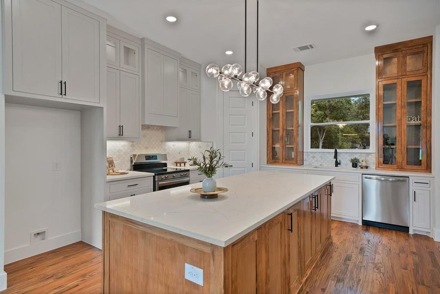 Kitchen featuring brown cabinetry, a kitchen island, backsplash, stainless steel appliances, and pendant lighting Kitchen featuring brown cabinetry, a kitchen island, backsplash, stainless steel appliances, and pendant lighting