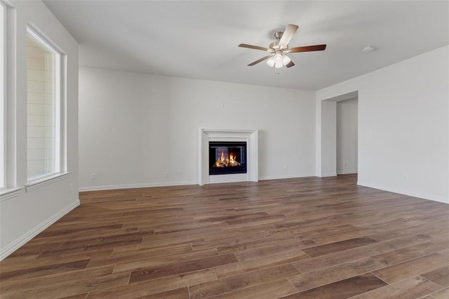 Unfurnished living room featuring wood finished floors, a glass covered fireplace, and a ceiling fan