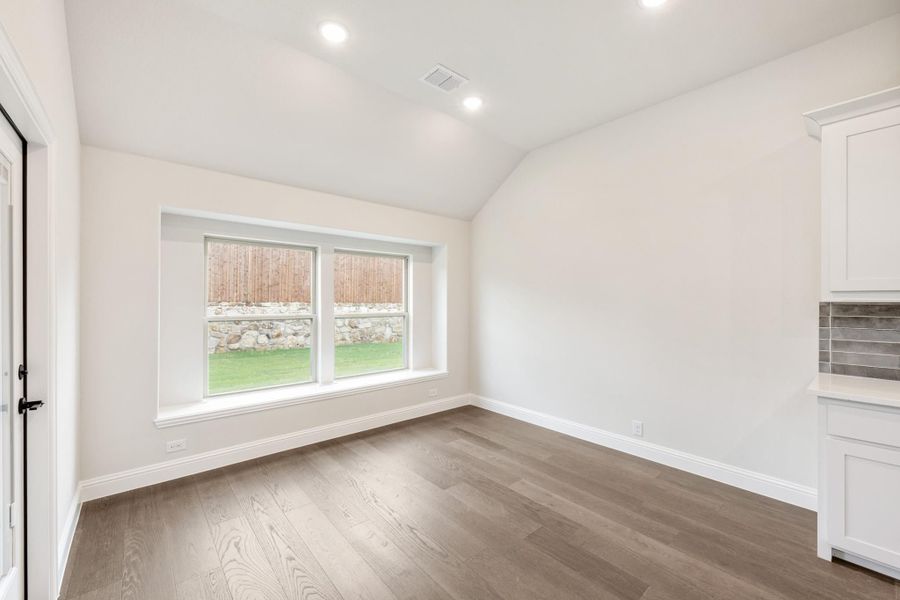 Empty room with vaulted ceiling, hardwood floors, and double windows overlooking a backyard Empty room with vaulted ceiling, hardwood floors, and double windows overlooking a backyard