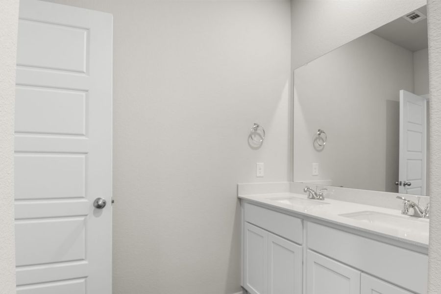 Image of a primary bathroom with cream walls, white cabinets and jack and jill vanity, and a large mirror