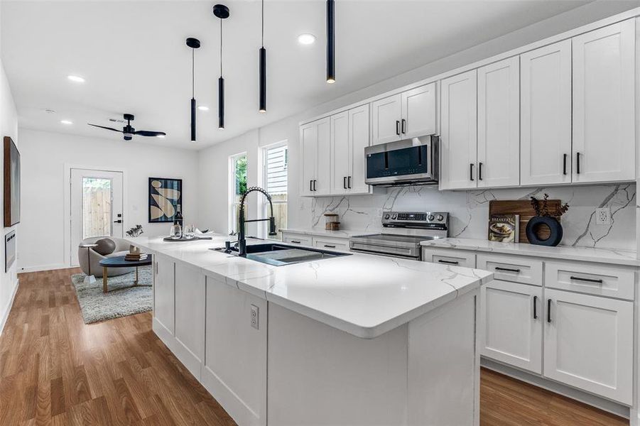 Kitchen featuring tasteful backsplash, white cabinetry, an island with sink, light wood-style floors, and stainless steel appliances Kitchen featuring tasteful backsplash, white cabinetry, an island with sink, light wood-style floors, and stainless steel appliances