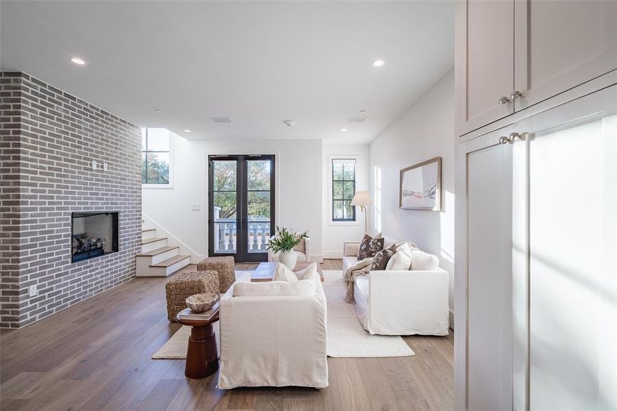 Living room with a brick fireplace, light wood-type flooring, and french doors