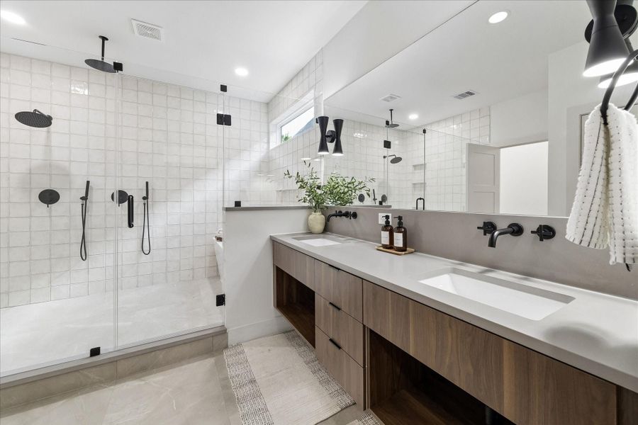 Spa inspired primary bath blends luxury with thoughtful design. A floating double vanity with quartz countertops, dual undermount sinks, and matte black wall mounted fixtures delivers a clean, contemporary aesthetic, while designer sconces and a full width mirror enhance the sense of space.