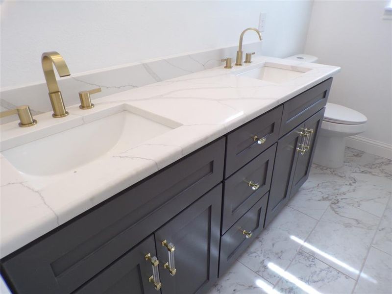 Bathroom with toilet, tile patterned flooring, and dual bowl vanity