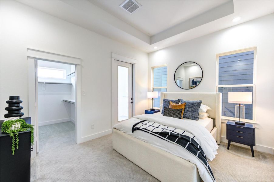 Primary bedroom located on the third floor featuring 10-ft coffered ceilings, a private ensuite balcony, and dual walk-in closets with box shelving. Pre-wired for a ceiling fan and 5.1 surround sound, with carpeted flooring and a private ensuite bathroom.