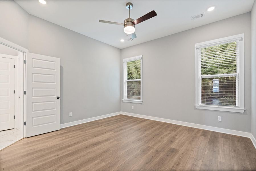 Spacious room featuring wood-finish flooring, two windows with blinds, a ceiling fan, and recessed lighting Spacious room featuring wood-finish flooring, two windows with blinds, a ceiling fan, and recessed lighting