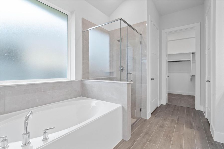 This alternate view of the primary bathroom showcases a walk-in shower with a stylish tile surround, a separate garden tub perfect for unwinding after a long day, and a large rain glass window that provides natural light while maintaining privacy.