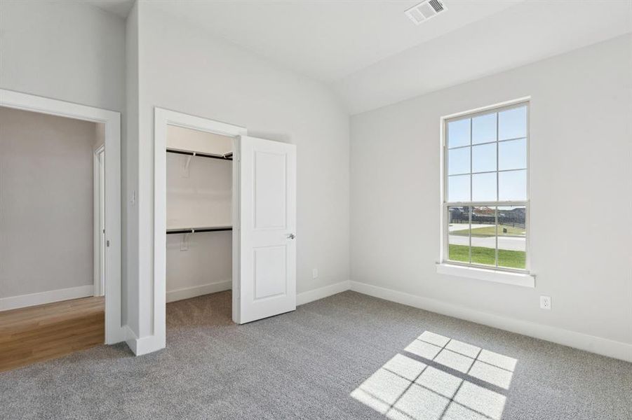 Unfurnished bedroom with light colored carpet, a walk in closet, and vaulted ceiling